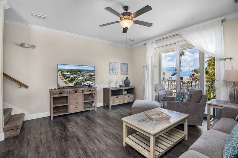 Unwind in a bright coastal living room with comfortable seating, a television, and glass doors opening toward the balcony.