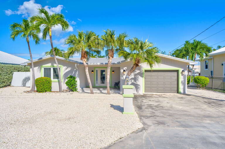 Daytime exterior front view of  Florida Keys vacation rental showcasing curb appeal and tropical landscaping. Daytime exterior front view of  Florida Keys vacation rental showcasing curb appeal and tropical landscaping.
