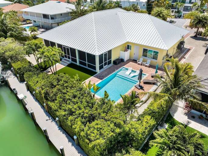 This aerial view captures the canal front home, private pool, screened outdoor area, tropical yard, and waterfront dock.