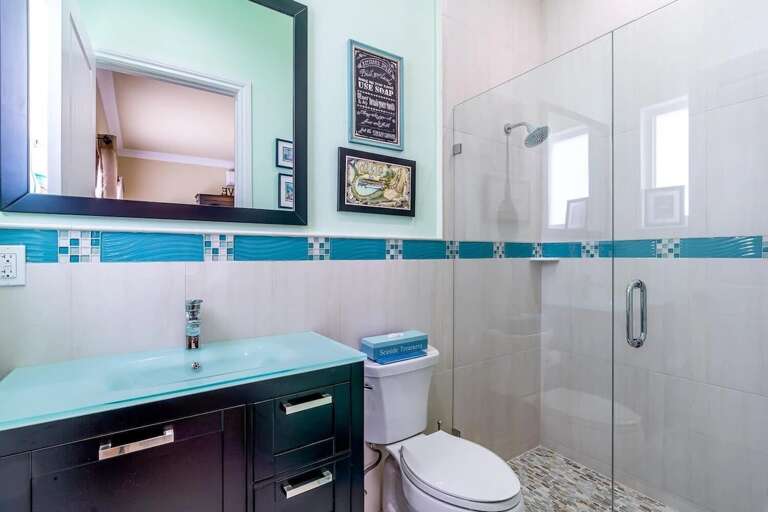 A bright guest bathroom with turquoise accents, a spacious vanity, and a glass-enclosed walk-in shower.