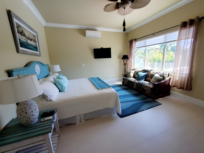 This comfortable bedroom features blue coastal furnishings, a loveseat, television, ceiling fan, and large window.