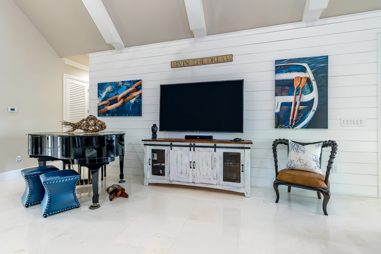 A large television, piano, storage console, and colorful Florida Keys artwork create a welcoming entertainment area.