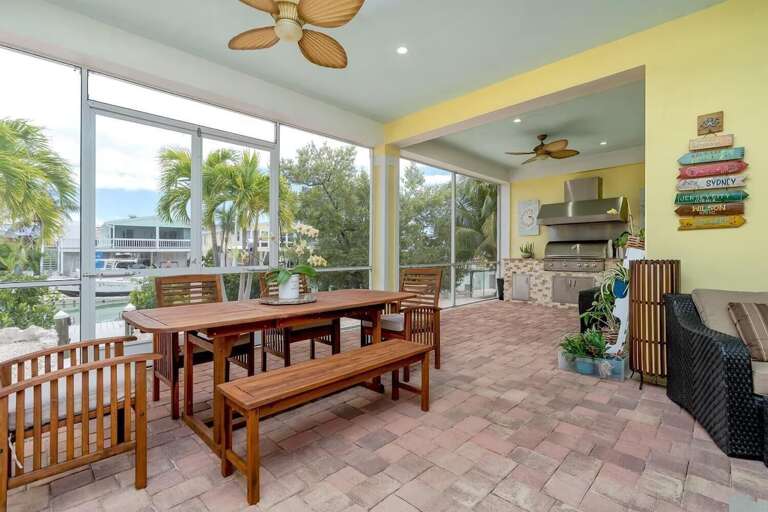 A large wooden dining table provides a comfortable setting for open-air meals inside the home's screened patio.