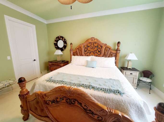 An ornate carved-wood bed, bedside tables, and soft green walls create a warm and comfortable guest retreat.