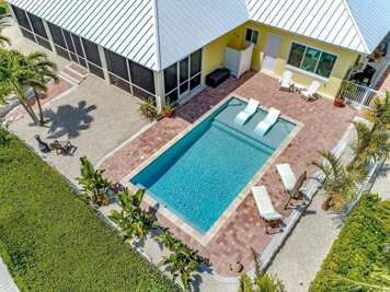An overhead view highlights the rectangular pool, sun shelf, lounge chairs, brick patio, and screened lanai.