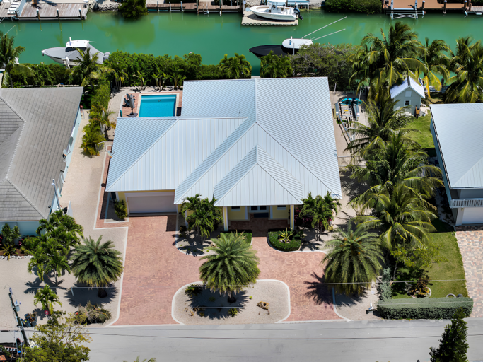 An overhead view showcases Casa Del Sol's metal roof, circular brick driveway, tropical landscaping, private pool, and canal front location.