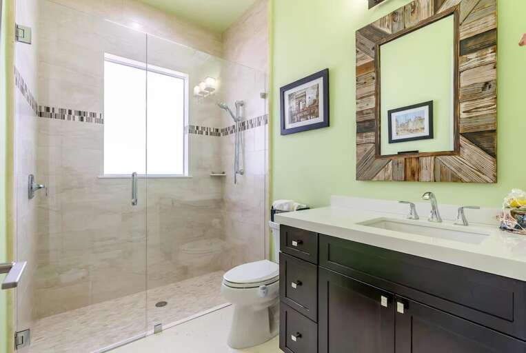 A spacious tiled shower, wide countertop, dark vanity, and decorative mirrors complete this Marathon guest bathroom.