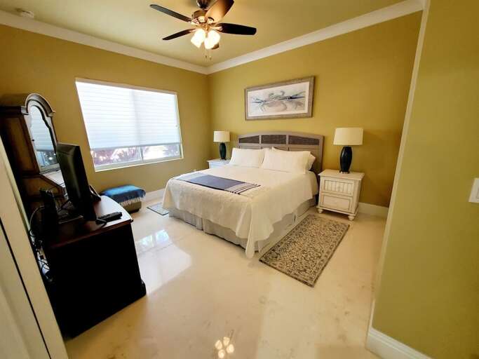 A welcoming bedroom with neutral bedding, bedside tables, a dresser, television, and warm yellow walls.