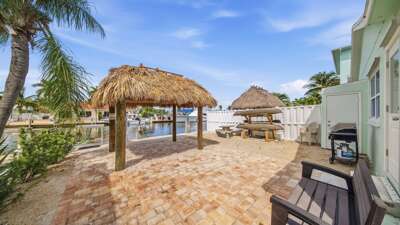 The brick patio offers shaded tiki areas, outdoor seating, a grill, and a relaxing setting for enjoying the Florida Keys weather.