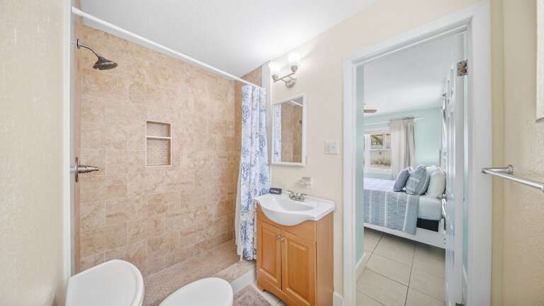 This convenient ensuite bathroom features a tiled walk-in shower, wood vanity, pedestal sink, and direct bedroom access.