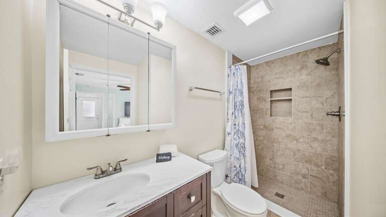 A long vanity, large mirror, tiled walk-in shower, and bright overhead lighting provide plenty of room for guests.