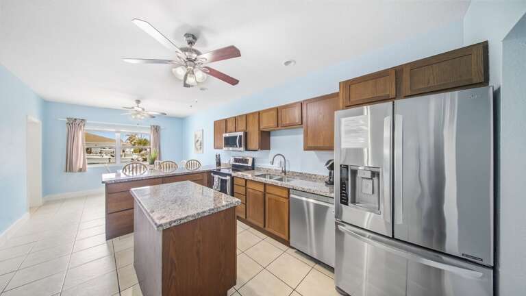 Prepare vacation meals in a bright kitchen featuring granite countertops, a center island, wood cabinetry, and stainless-steel appliances.
