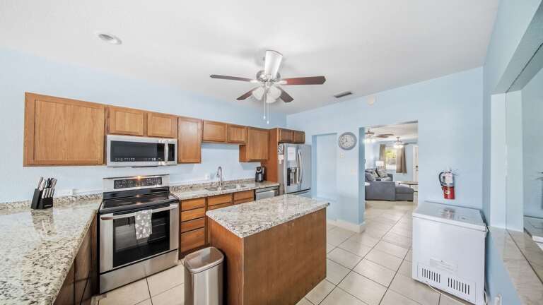 Prepare vacation meals in a bright kitchen featuring granite countertops, wood cabinetry, a center island, and stainless-steel appliances.