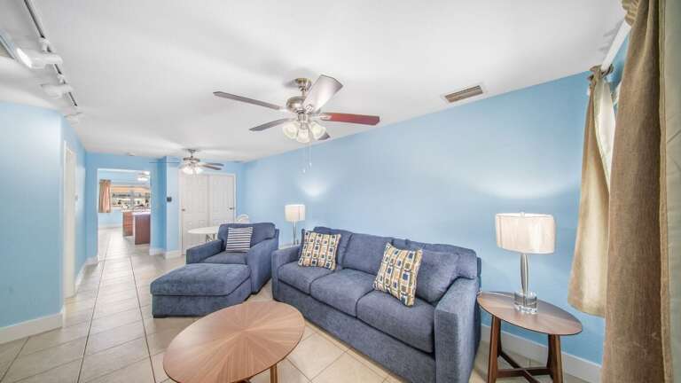 Relax on a spacious blue sectional in this bright Florida Keys living room featuring coastal colors, a ceiling fan, and comfortable seating.