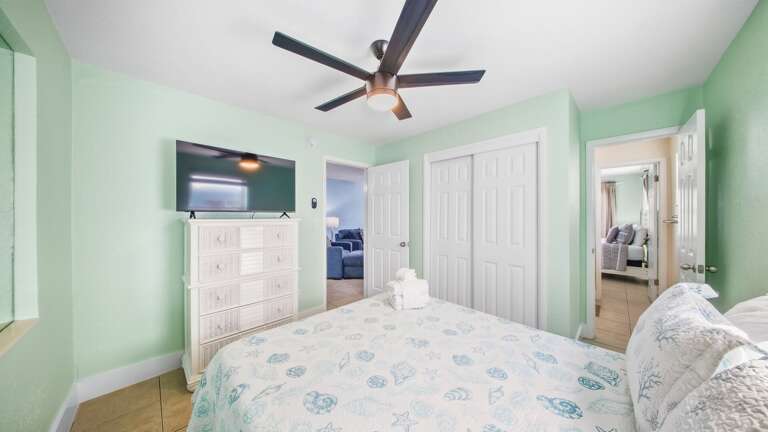 This relaxing bedroom features a comfortable bed, white dresser, television, ceiling fan, and convenient closet storage.