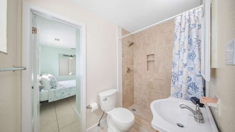 A spacious tiled shower, built-in wall niches, pedestal sink, and bright finishes complete this comfortable guest bathroom.