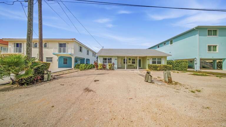 A wide street view displays the covered porch, generous parking area, tropical landscaping, and quiet residential setting.