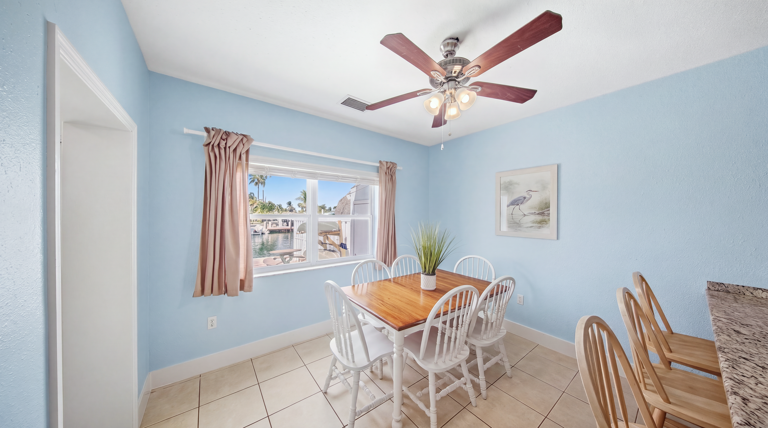 A wooden table with white chairs sits beside a sunny window, providing an inviting setting for meals and conversation.