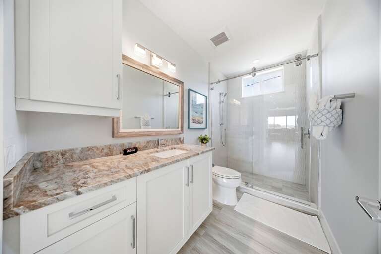 This bright bathroom includes a granite countertop, spacious vanity, large mirror, and glass-enclosed shower-and-tub combination.