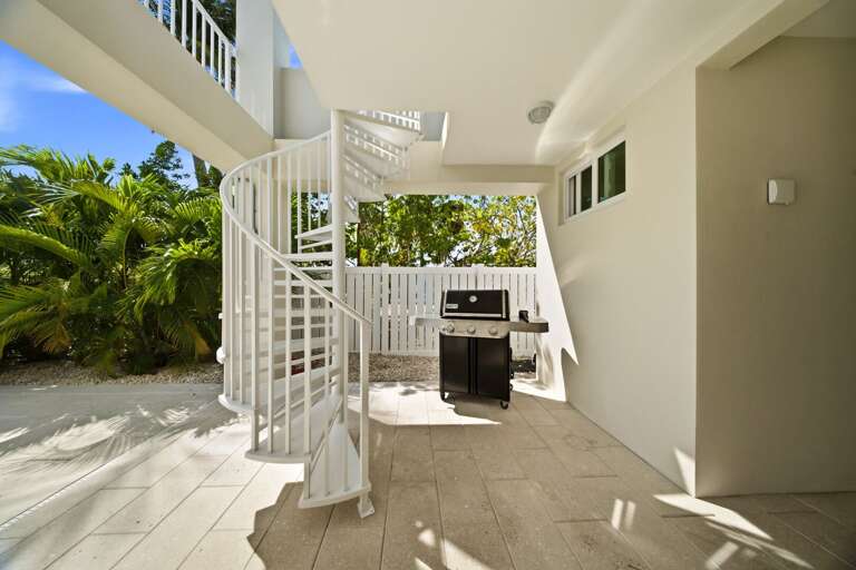 A shaded ground-level patio features a grill, spiral staircase, and plenty of space for casual outdoor entertaining.