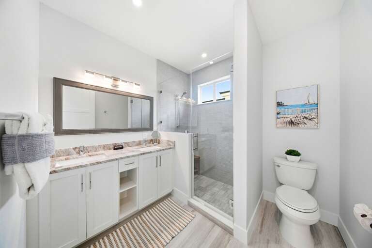 This bright bathroom features a spacious vanity, large mirror, generous storage, and a glass-enclosed walk-in shower.