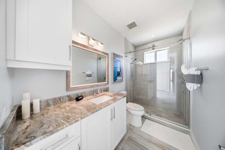 A granite-topped vanity, large mirror, white cabinetry, and glass-enclosed shower complete this bright guest bathroom.