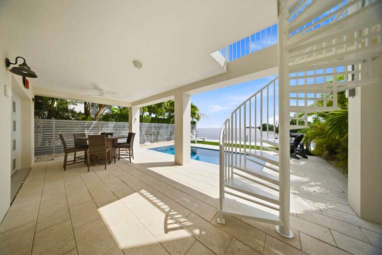 This covered outdoor area offers dining space, pool access, and a spiral staircase connecting the home's waterfront levels.