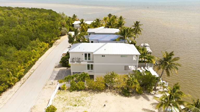 This aerial view highlights the home's coastal location, multi-level design, tropical surroundings, and proximity to open water.