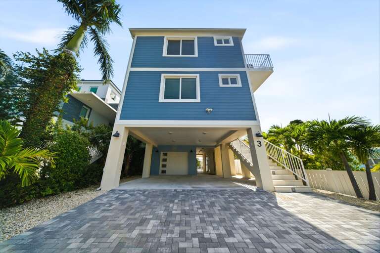 This front view showcases the elevated coastal design, spacious driveway, covered parking, and tropical Florida Keys setting.