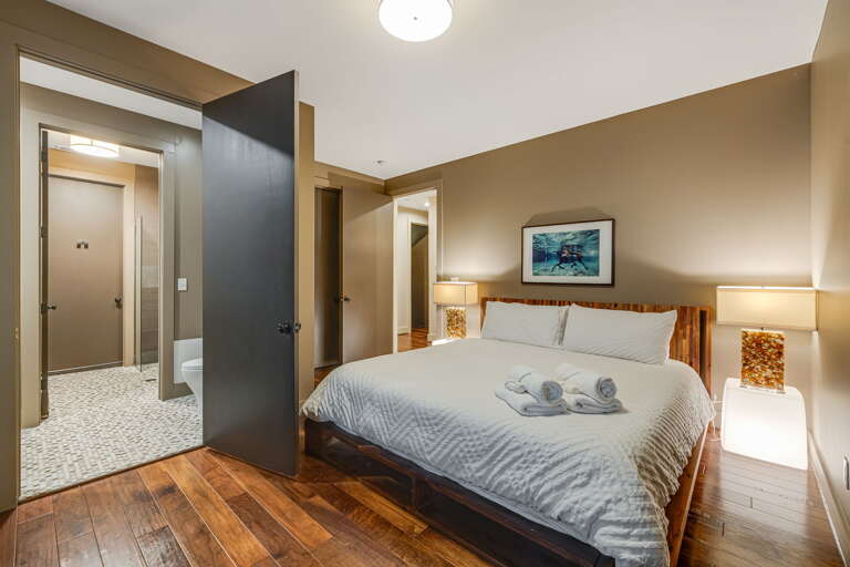 Sink into plush linens and soft lighting after a day of adventure. Your suite features rich wood floors, a welcoming bed dressed with fresh towels, and warm accents that make rest feel effortless.