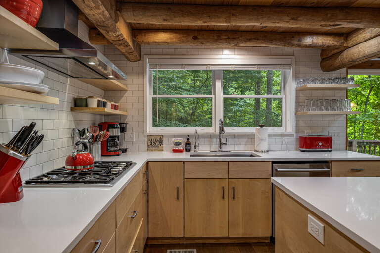 Step into your private chef's kitchen, where rustic log beams meet modern design. Cook gourmet meals at the gas range, enjoy forest views through the window, and gather around the spacious counters surrounded by warm wood and natural light.