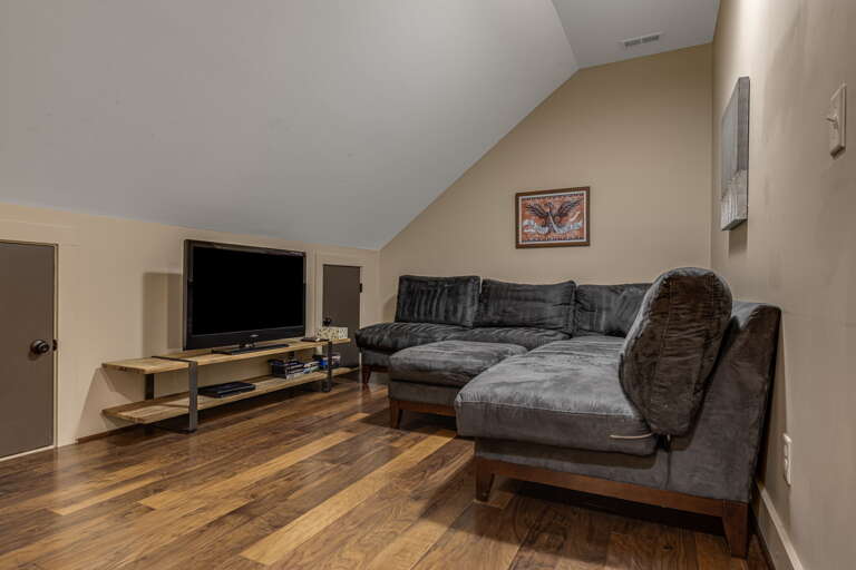 Sink into the plush sectional in your private living space, where vaulted ceilings and rich wood floors create a warm, relaxing atmosphere perfect for movie nights or quiet conversation.