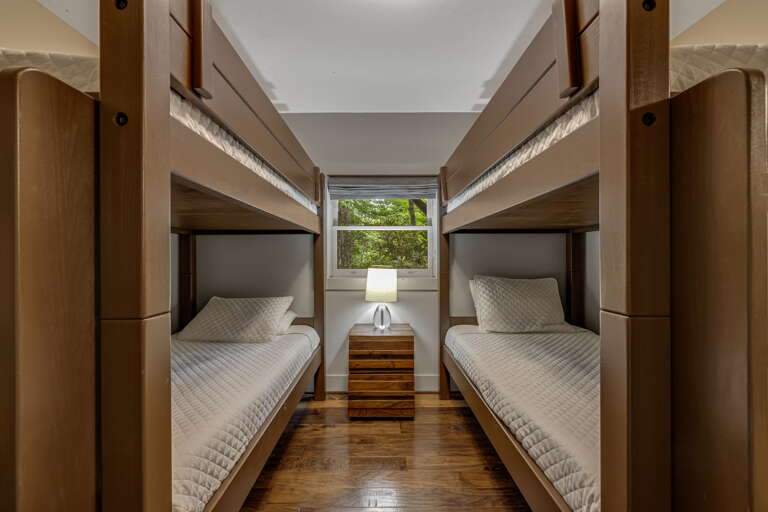 This cozy bunk room provides flexible sleeping arrangements, with four comfortable beds tucked into warm wood frames and a leafy garden view through the window—perfect for families or groups traveling together.