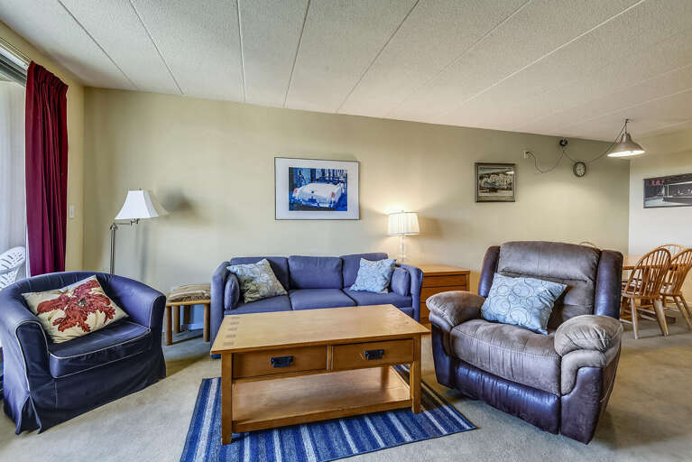 Living Space With Plush Seating, Striped Rug, And Hanging Landscape Artwork