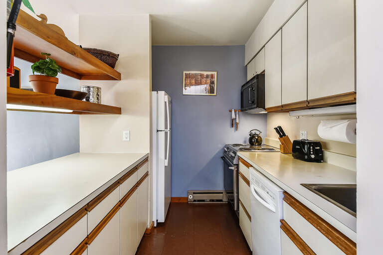 Compact Kitchen With White Cabinetry And Wooden Shelves, Featuring Full-sized Fridge And Stove