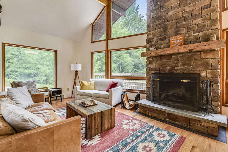 Vacation Rental Living Area With Stone Fireplace, Large Windows, And Forest View