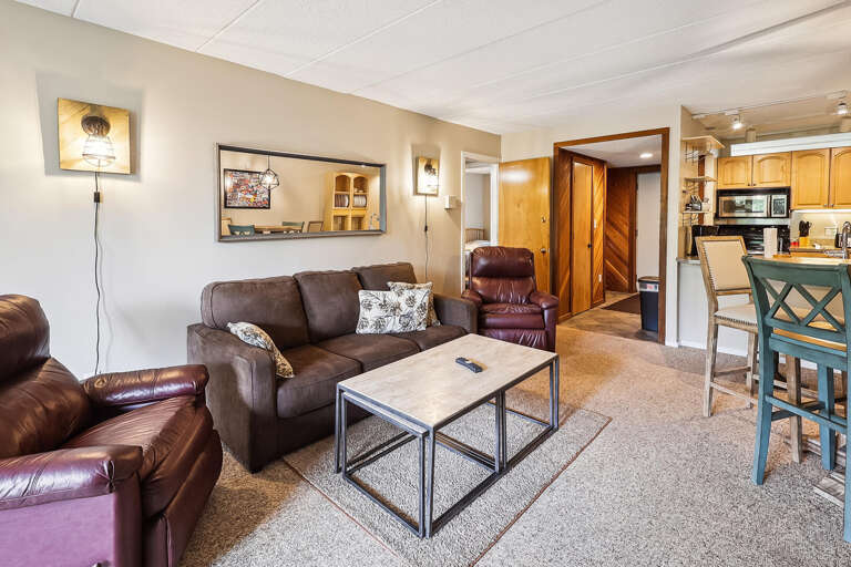 Living Space With Brown Sofas, Glass Table, And Kitchen View