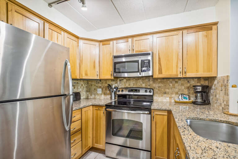 Kitchen With Stainless Steel Stove And Refrigerator, Light Wooden Cabinets, And Granite Countertops