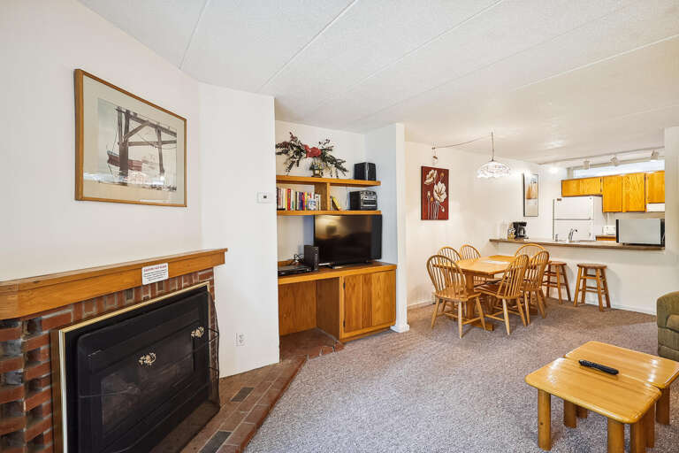 Living Room Leading To Kitchen In Vacation Rental With Dining Area, Fireplace, And Entertainment Setup