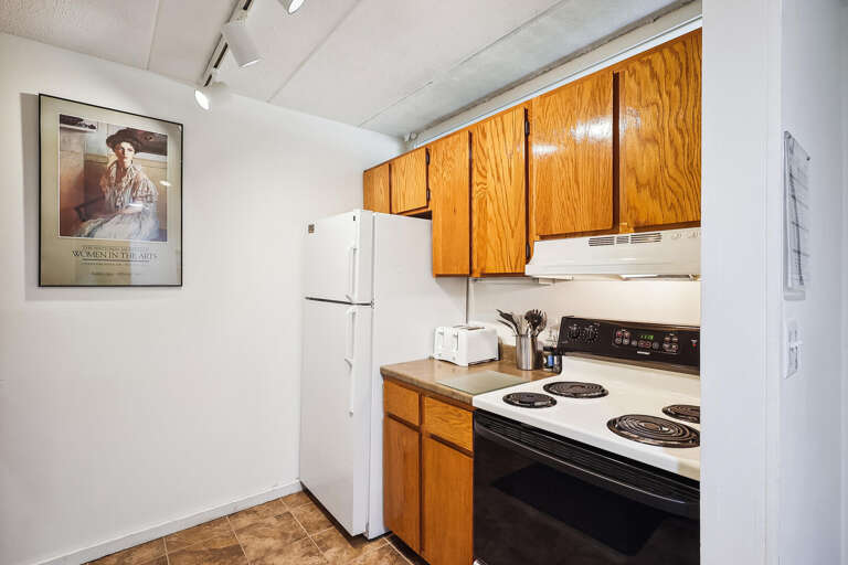 Small Kitchen Space With White Appliances And Wooden Cabinets