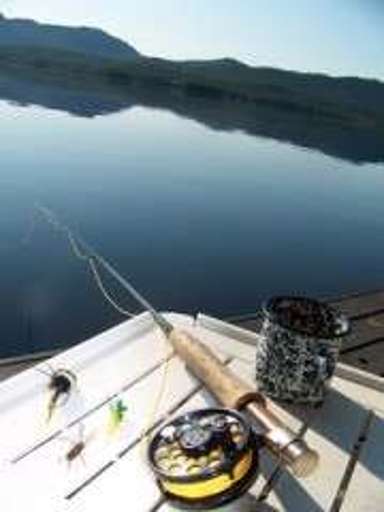 Fishing Gear On A Dock Overlooking A Calm Lake With Mountains In The Background
