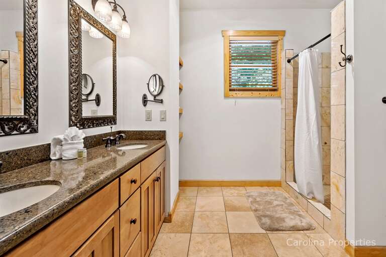 The adjoining full bathroom has a double sink and a walk-in, tiled shower with a seat 