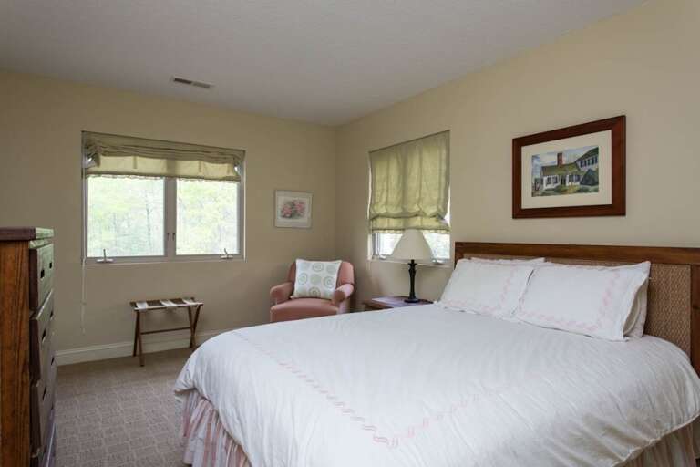 One of the bedrooms has a queen bed with a cozy chair, bureau, and windows.