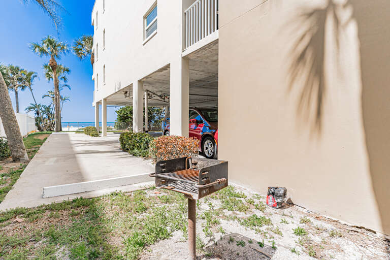 Beachfront property with covered parking, BBQ grill, and tropical landscaping near the sandy shore.