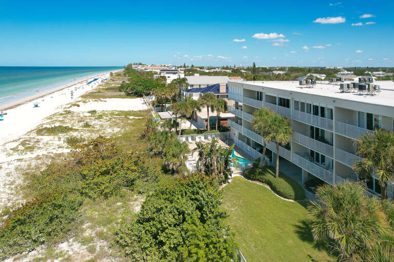 Beachfront property with pristine white sand beaches, tropical landscaping, and multi-story accommodation buildings near the Gulf Coast.
