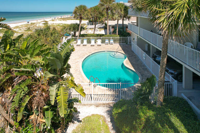 Beachfront property featuring a curved swimming pool surrounded by tropical palms and white sand beaches.