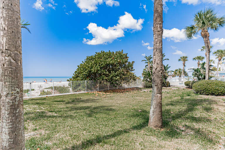Tropical beachfront setting with palm trees and expansive lawn area leading to pristine sandy shores and crystal-clear waters beyond.