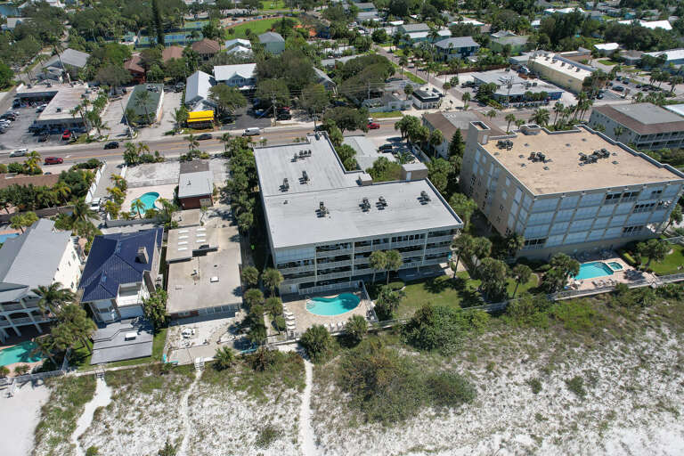 Aerial view of beachfront resort buildings nestled among palm trees, with multiple pools and direct beach access in a tropical coastal setting.