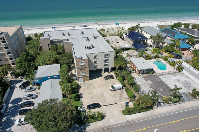 Beachfront property offering stunning aerial perspective of pristine white sand beach and turquoise waters, surrounded by tropical palm trees and neighboring vacation homes.