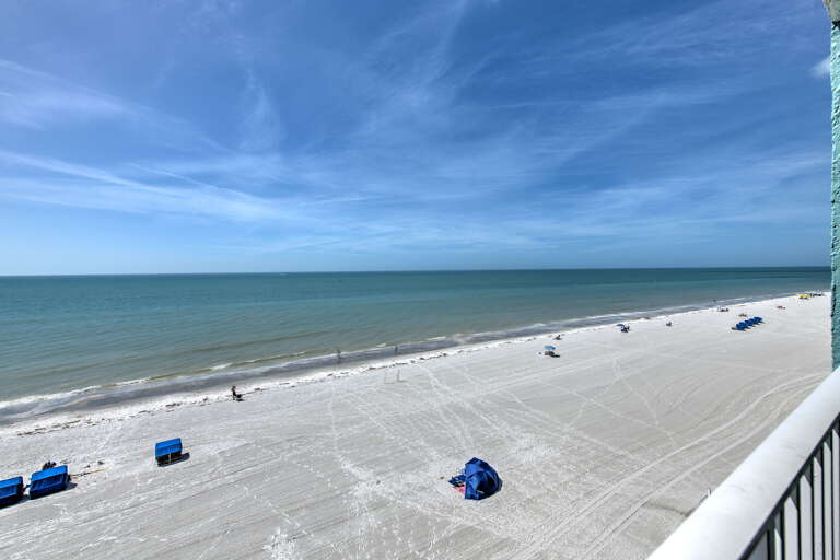 Pristine white sand beach stretches endlessly along emerald waters, visible from the property balcony.